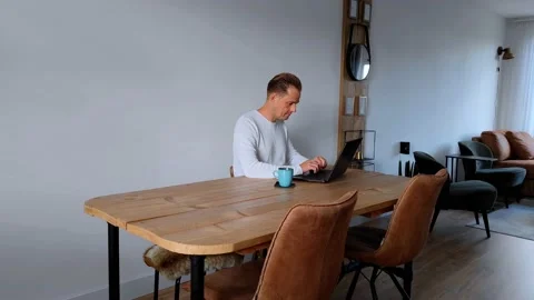 Smiling man is working from home on a table with his laptop Stock Footage 211903439