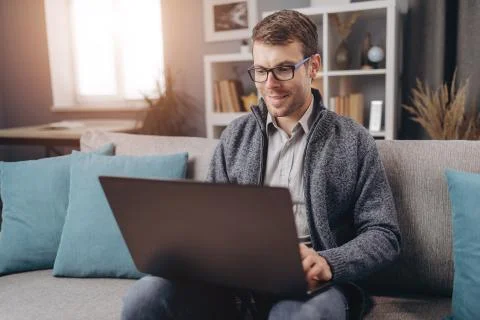 Smiling man working on laptop while sitting on couch Stock Photos