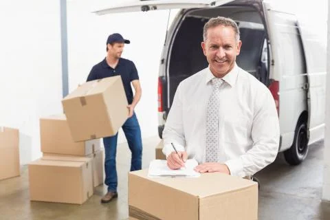 Smiling manager standing behind stack of cardboard boxes Stock Photos