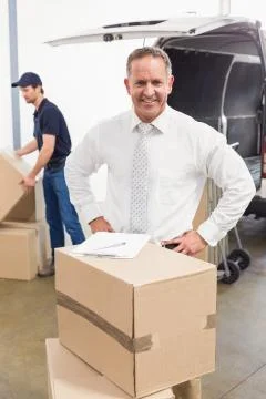Smiling manager standing behind stack of cardboard boxes Stock Photos