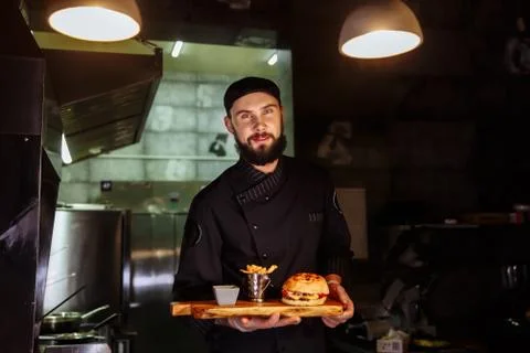 Smiling master chef in uniform looking at camera, holding plate with served Stock Photos