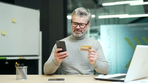 Smiling mature gray haired bearded businessman wearing glasses is typing credit  Stock Footage 232575309