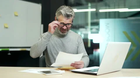 Smiling mature gray haired bearded man in glasses reading letter with good news  Stock Footage 232575900