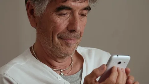 Smiling mature man focused on typing on  his smartphone- indoor Stock Footage 77739119