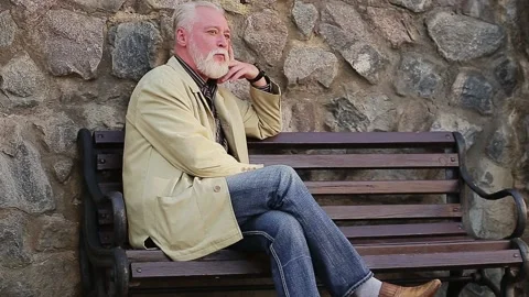 Smiling mature man sitting on bench by stone wall Stock Footage 168911022