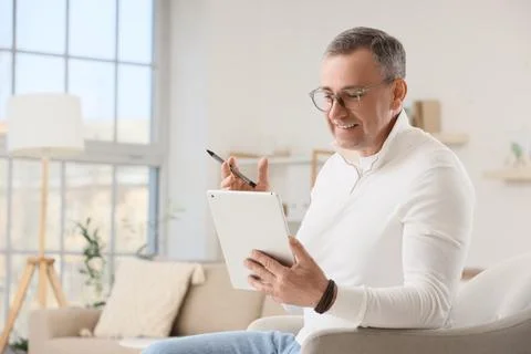 Smiling mature man using digital tablet and stylus pen for online learning or Stock Photos