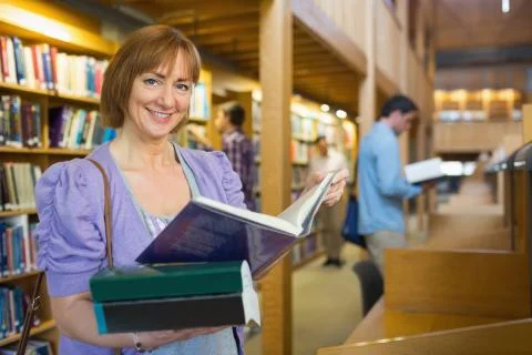 Smiling mature student with men in the background at library Stock Photos