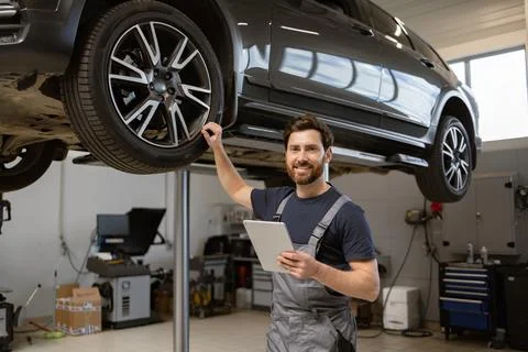 Smiling mechanic using tablet in auto repair shop with car on lift 스톡 사진