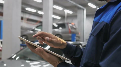 Smiling mechanic using a tablet pc at the repair garage service Stock Footage 67684376