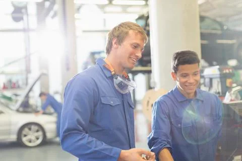 Smiling mechanics using computer in auto repair shop Stock Photos