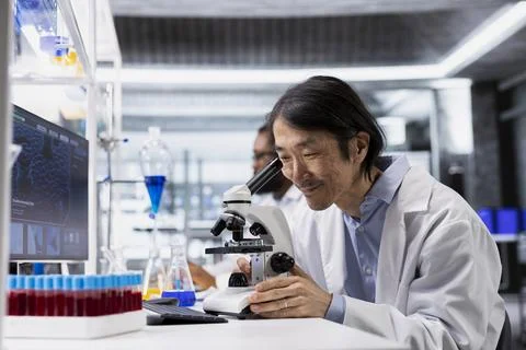 Smiling microscopist using microscope, pleased by sample observation results Stock Photos