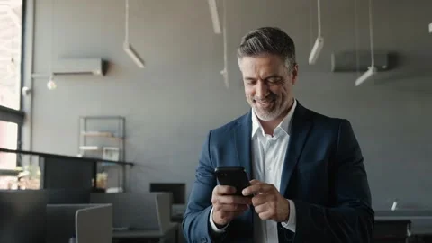 Smiling mid aged male ceo executive wearing suit using cell phone in office. Stock Footage 242371815