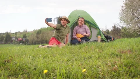 Smiling middle-aged couple next to camp tent have video call with friends via sm Stock Footage 309540195