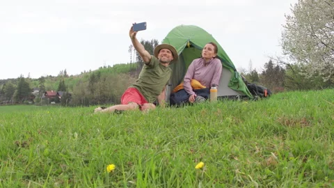 Smiling middle-aged couple next to camp tent taking selfies together using smart Stock Footage 309592053
