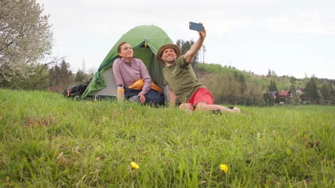 Smiling middle-aged couple next to camp tent taking selfies together using smart Stock Footage 317914993