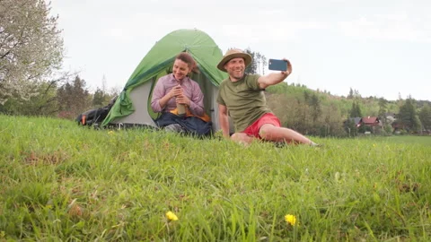 Smiling middle-aged couple next to camp tent taking selfies together using smart Stock-Footage 321847126