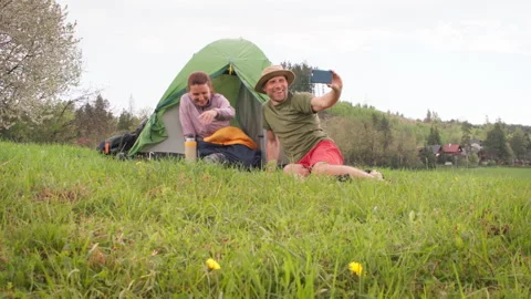 Smiling middle-aged couple next to camp tent taking selfies together using smart Video stock 327179915
