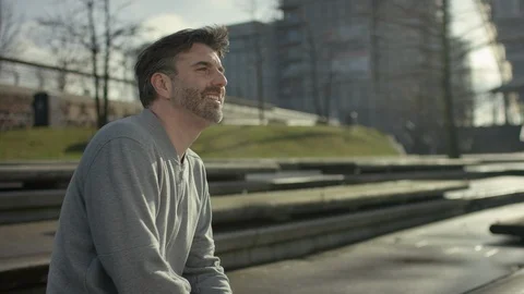 Smiling middle aged man is siiting on a bench in modern urban city in autumn Video stock 97848471