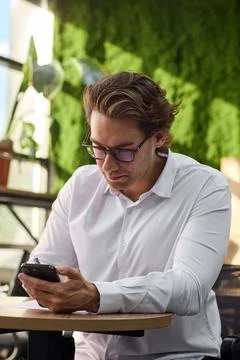 Smiling middle aged man in white shirt sits at round table writing on paper Stock-Fotos