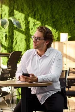 Smiling middle aged man in white shirt sits at round table writing on paper Stock-Fotos