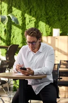Smiling middle aged man in white shirt sits at round table writing on paper Stock-Fotos