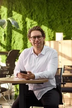 Smiling middle aged man in white shirt sits at round table writing on paper Stock-Fotos