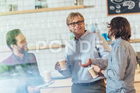 Smiling middle aged men drinking coffee and talking in cafe Stock Photos
