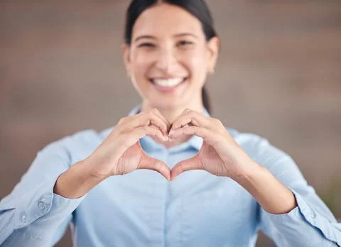 Smiling mixed race businesswoman standing alone and using hand gestures to make Stock Photos