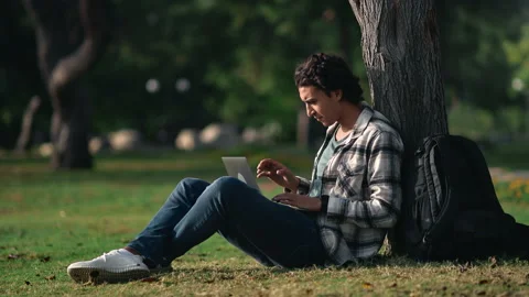 Smiling mixed race casual student guy e learning remotely use laptop outdoor at Stock Footage 221013226