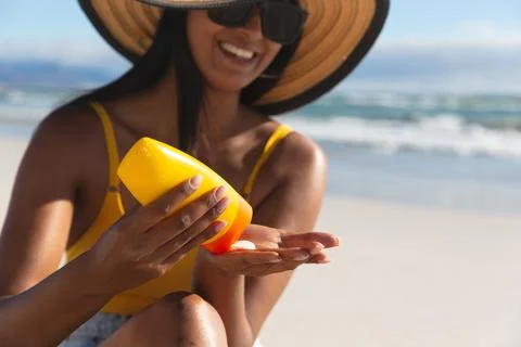 Smiling mixed race woman on beach holiday using sunscreen cream Stock Photos