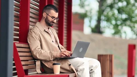 Smiling modern freelancer man working chatting online use laptop wooden bench Stock Footage 244080992