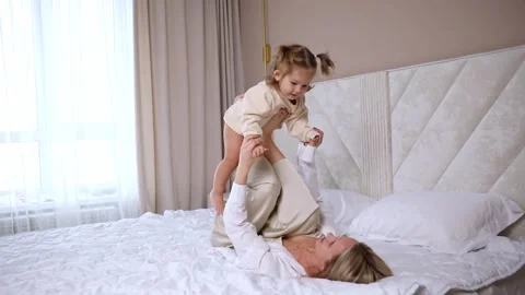 Smiling mom lying on bed hold excited small girl child on legs up in air.  Stock Footage 306889654