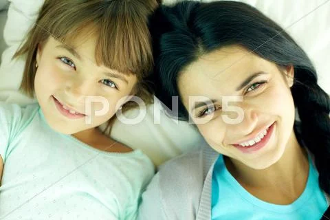 Smiling mother and her daughter lying in bed and looking at camera Stock Photos