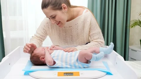 Smiling mother looking and stroking her little son while weighing him on digital Stock Footage 147421871