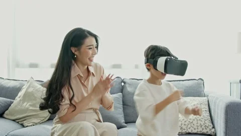 Smiling mother looking son playing games using virtual reality headset(VR) at Stock Footage 194812335