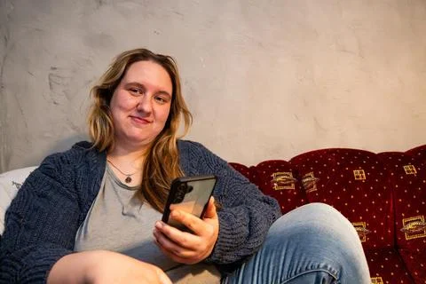 Smiling mother relaxing casually while using her smartphone in a cozy livin.. Stock Photos