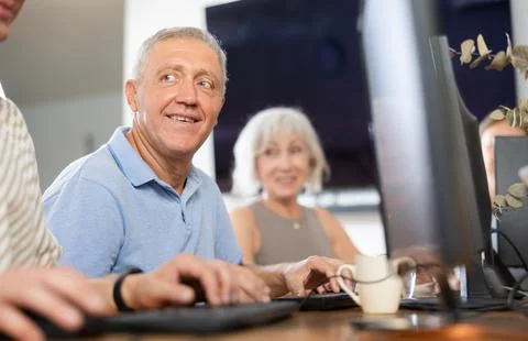 Smiling motivated older man using computer at internet cafe Fotos de archivo