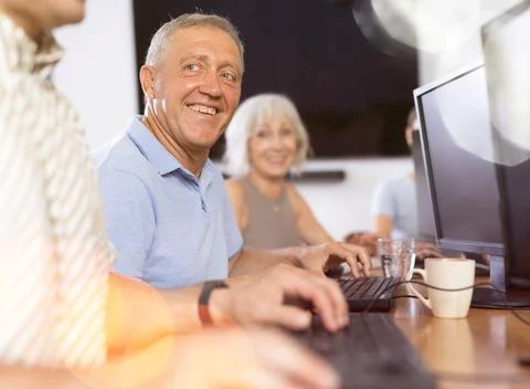 Smiling motivated older man using computer at internet cafe Fotos de archivo