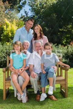 Smiling multi generation family sitting on a bench in park Stock Photos