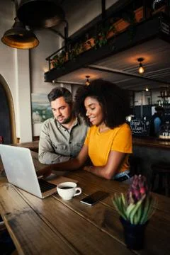 Smiling multi race couple browsing on laptop while drinking coffee in chic Stock Photos