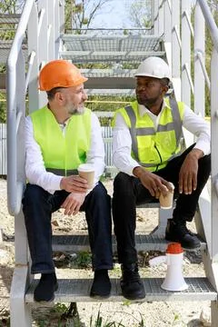 Smiling multicultural builders in hardhats looking at camera with smile and Stock Photos