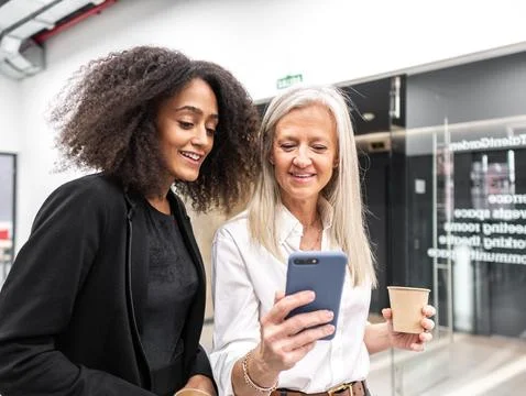 Smiling multiracial colleagues using smartphone and drinking takeaway coffe.. Stock Photos