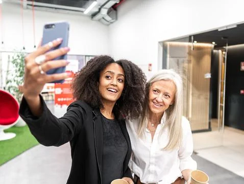 Smiling multiracial colleagues using smartphone and drinking takeaway coffe.. Stock Photos