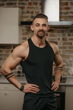 A smiling muscular man with a beard is posing in his apartment after a workou Stock Photos