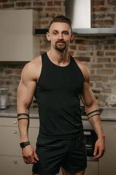 A smiling muscular man with a beard is posing in his apartment after a workou 스톡 사진