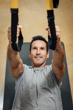 Smiling muscular man performing pull-up exercise using suspension trainer. Stock Photos
