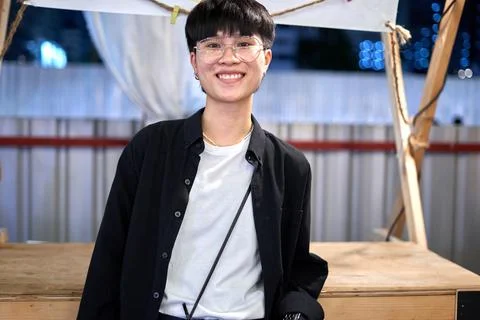 Smiling non-binary person with glasses standing in an urban night fair Stock Photos