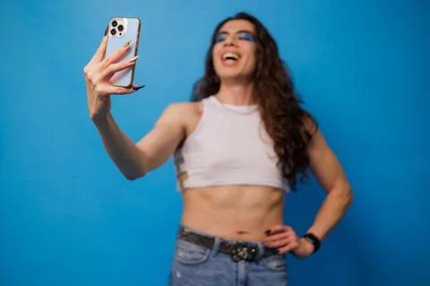 Smiling non-binary stylish person taking a photo with their cell phone on a b Stock Photos