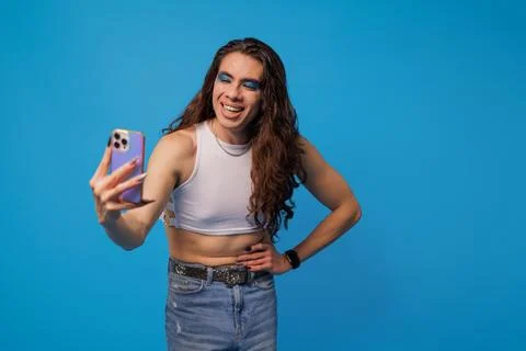 Smiling non-binary stylish person taking a photo with their cell phone on a b Stock Photos
