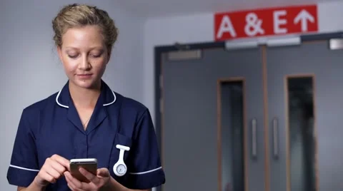 Smiling nurse using cell mobile phone in front of doors in hospital another n Stock Footage 59087311